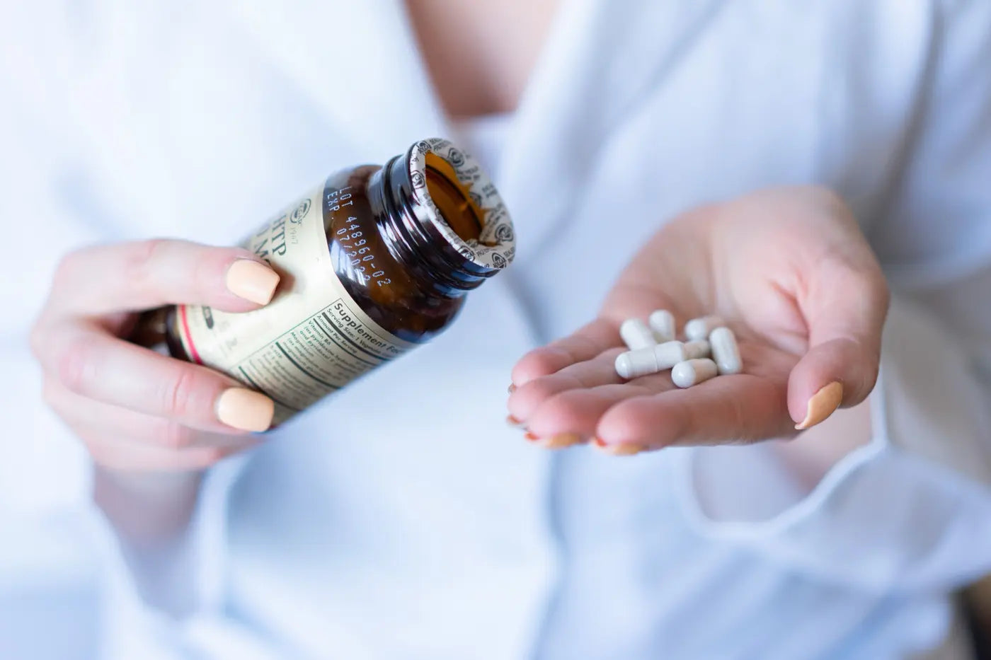 Capsules poured into a hand beside a supplement bottle showing its ingredients panel