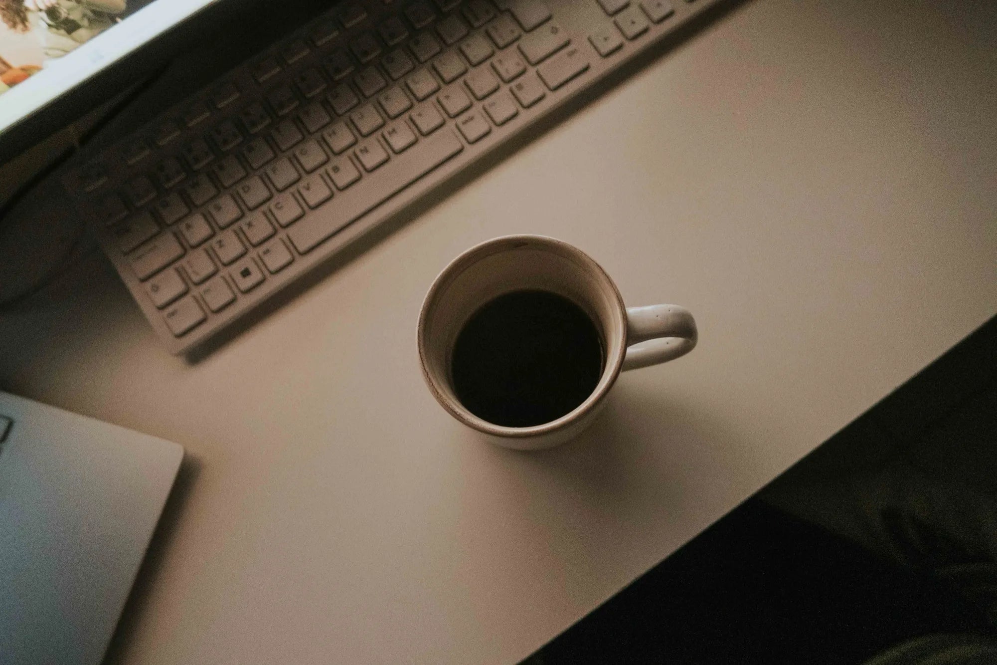 A mug of black coffee beside a keyboard on a desk in fading light