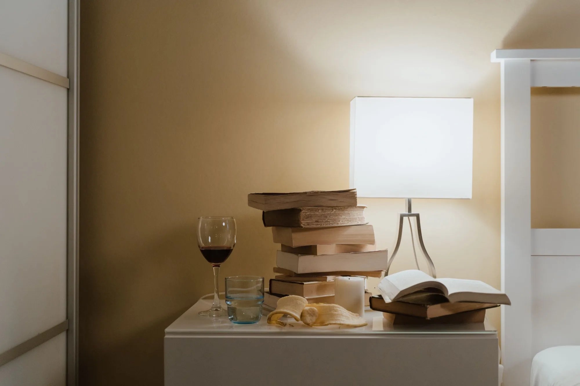 A glass of wine and a lamp on a bedside table at night